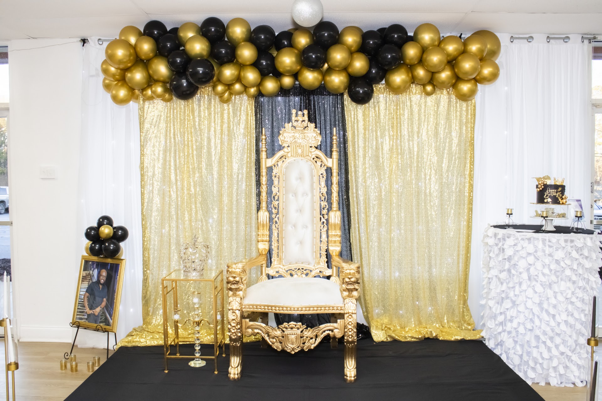 Gold throne chair with black and gold balloon decor at All & All Event Center